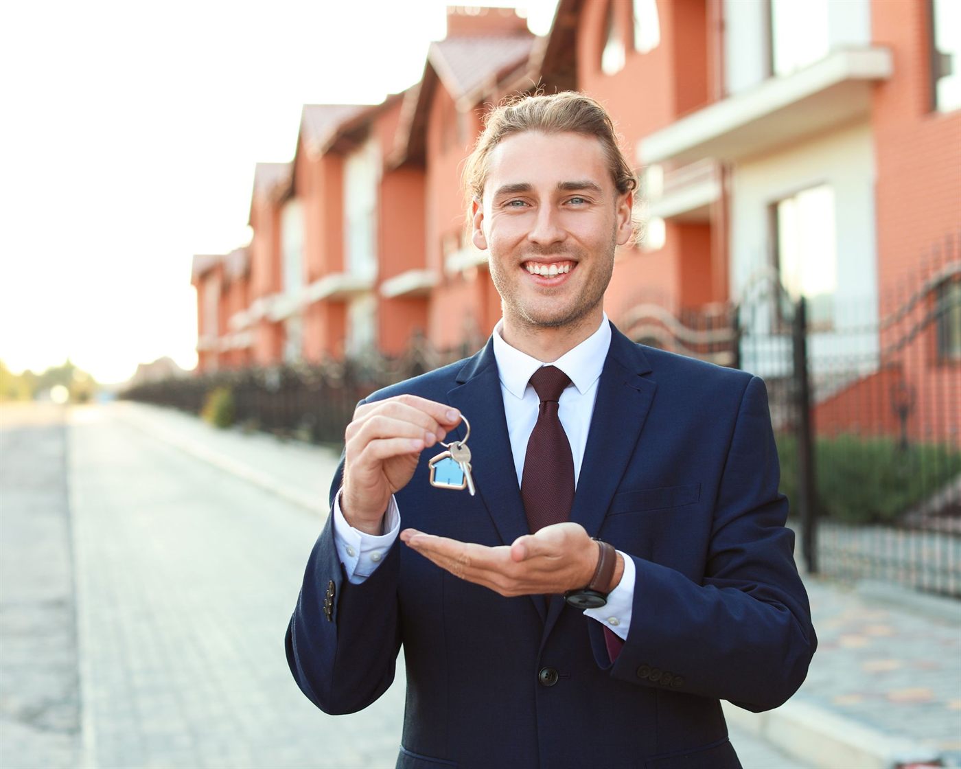 An agent holding out keys in front of a row of townhouses